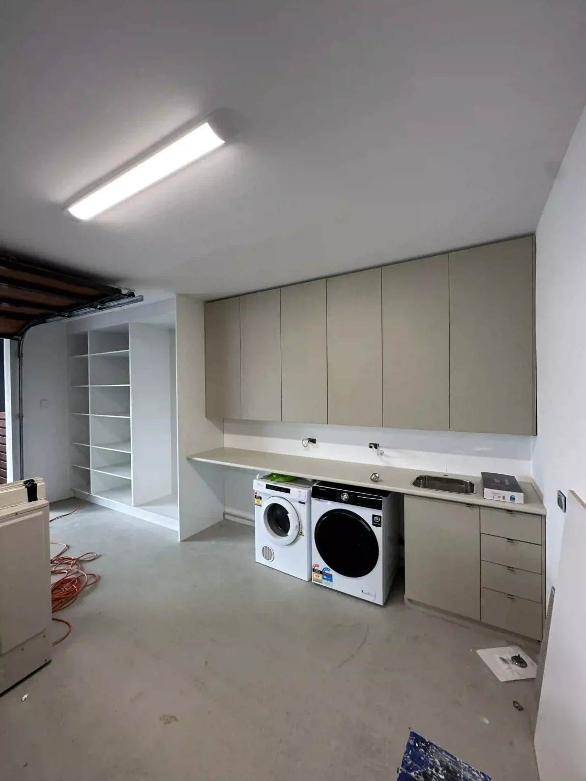 Finished laundry room in garage with white and light grey cabinetry, washing machine, dryer and storage shelving